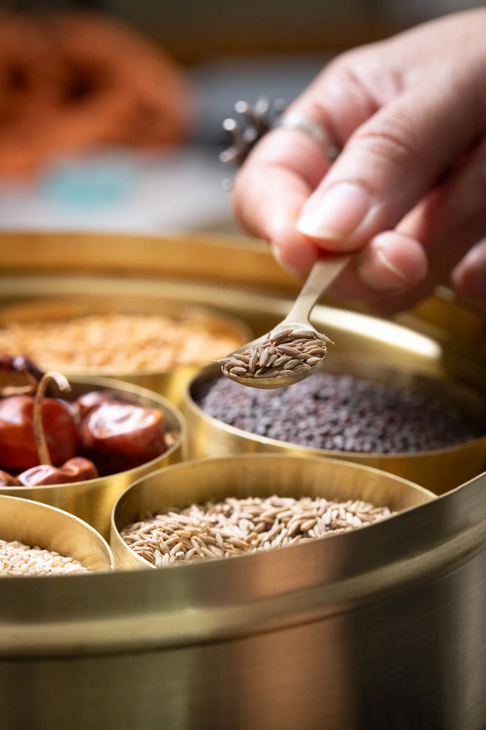 Taking a teaspoon of saunf from brass masala dabba