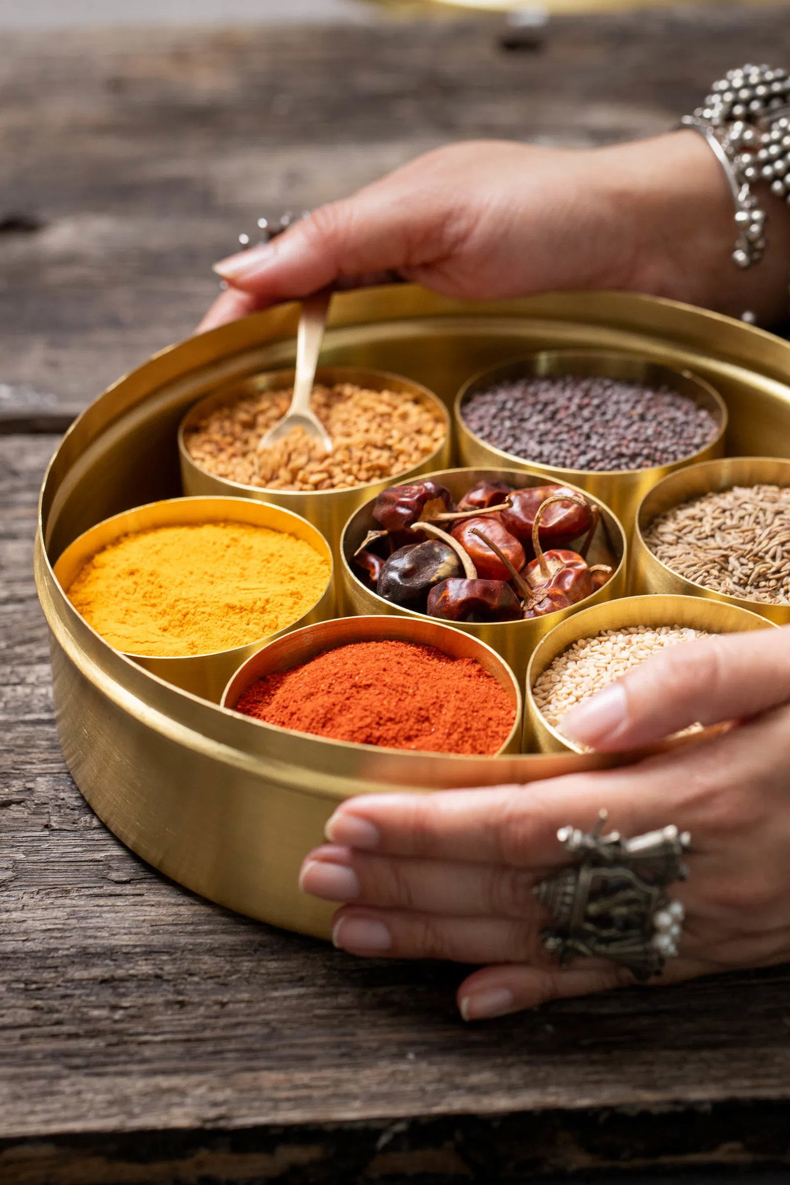 Hands holding a filled brass masala dabba